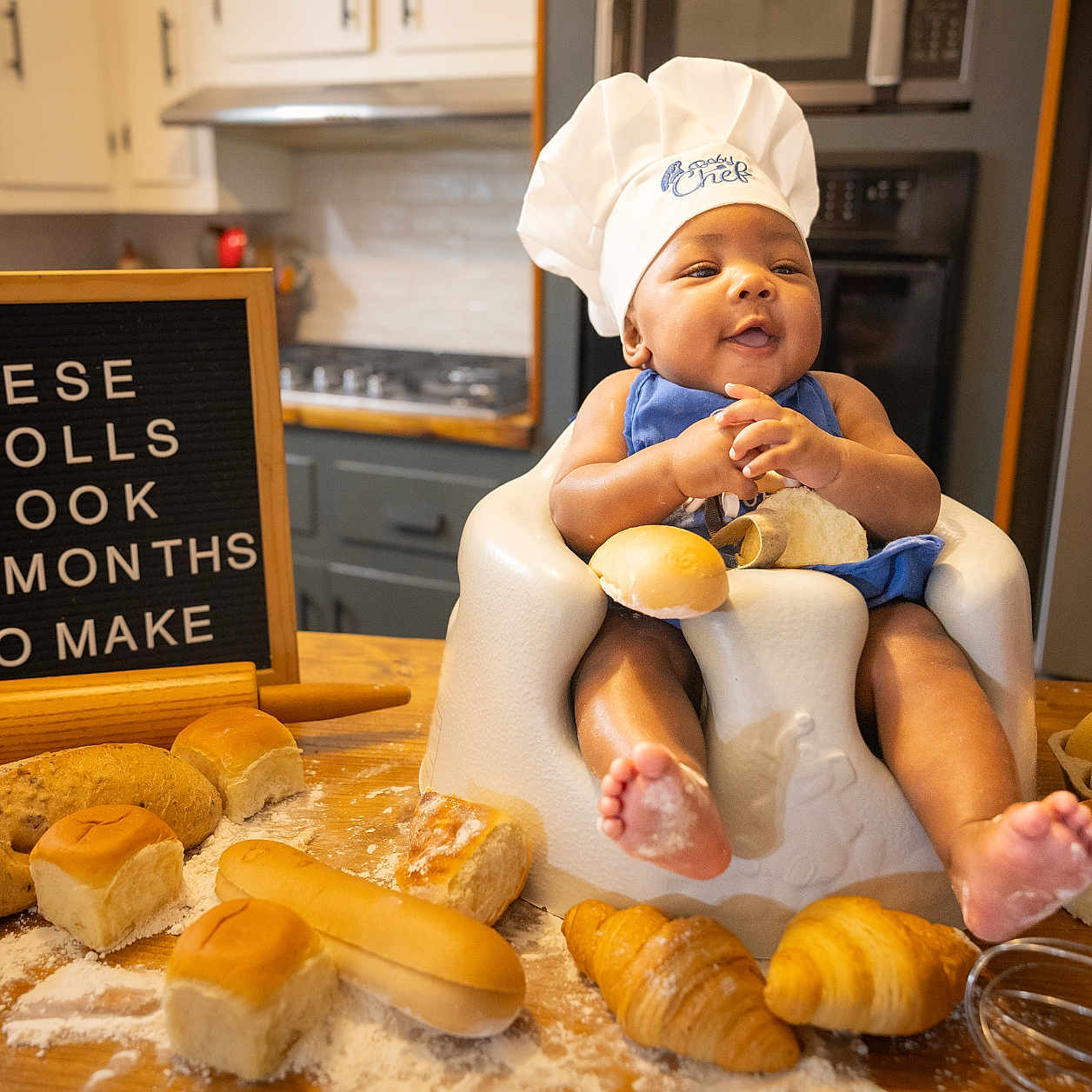 Jasai is registered to the contest to win money with this photo: apron, baby, bread, cabinet, chef_hat, cooking, countertop, cutting_board, eggs, flour, happy, high_chair, kitchen, oven, pastries, rolling_pin, rolls, smiling, table, wooden_table