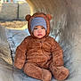 toddler, child, bear_costume, fuzzy_outfit, beanie, concrete_tunnel, outdoor, sitting, curious, serious_expression, cute, warm_clothing, portrait, baby, winter_wear, animal_ears, soft_texture, face, one_child, daylight