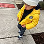 Trulynn joined the competition — help win amazing prizes! child, toddler, yellow_jacket, white_beanie, sidewalk, concrete, curious_expression, black_pants, black_shoes, urban, outdoor, casual_clothing, winter_wear, puffer_jacket, street, person, standing, daylight, fashion, closeup
