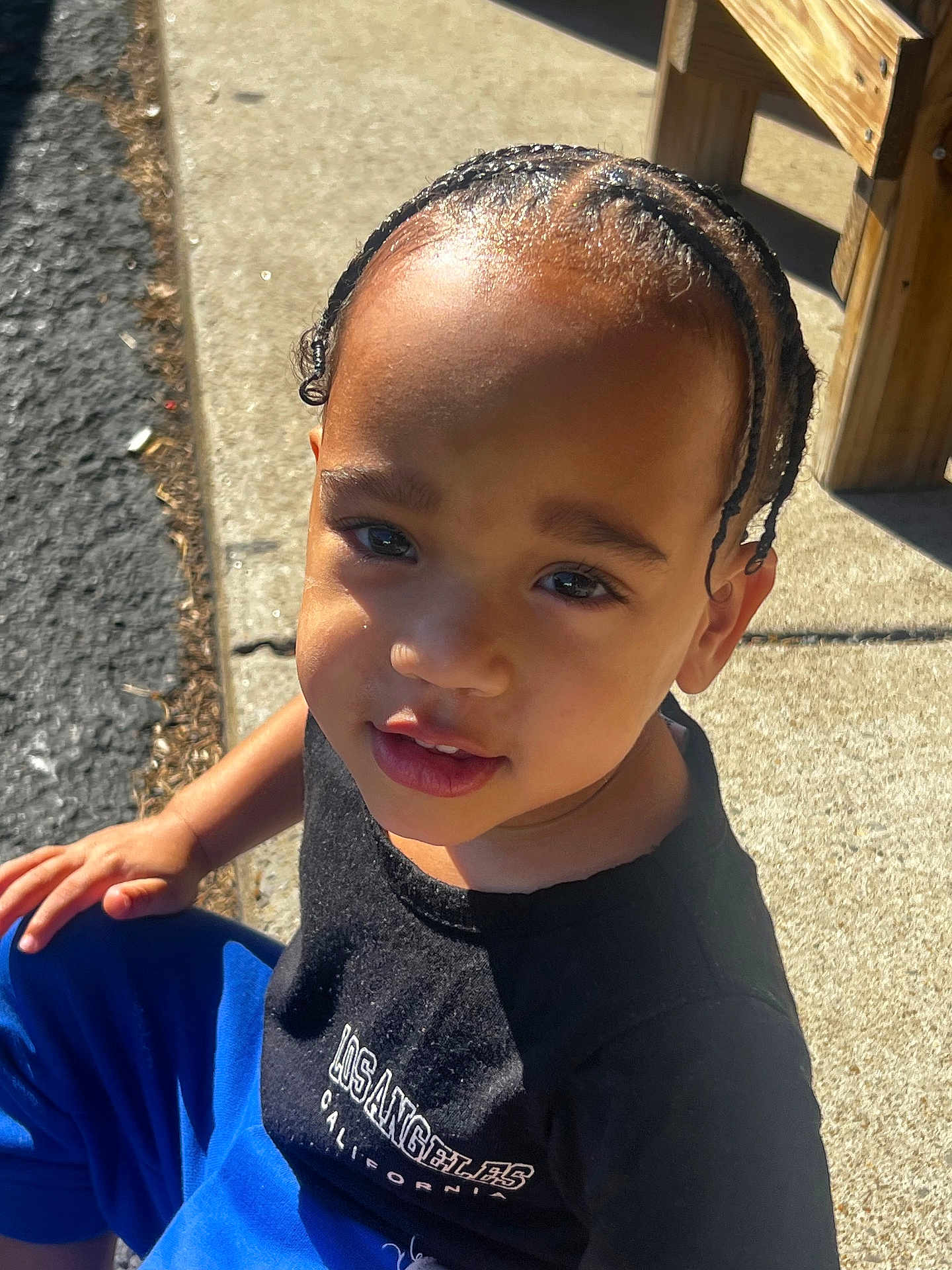 Trulynn joined the competition — help win amazing prizes! child, outdoor, sunlight, braided_hair, black_tshirt, blue_pants, bench, sidewalk, curious, smiling, portrait, person, casual_clothing, daylight, young_child, sitting, urban, street, cute, closeup