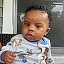 baby, child, onesie, teddy_bear_pattern, curly_hair, porch, window, screen_door, hand, clothing, infant, cute, face, expression, outdoor, person, sitting, holding, skin, young