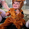 child, toddler, reindeer_costume, costume, smiling, happy, portrait, indoor, christmas, christmas_tree, holiday, living_room, carpet, playpen, brick_wall, toy_car, brown, sitting, festive, family