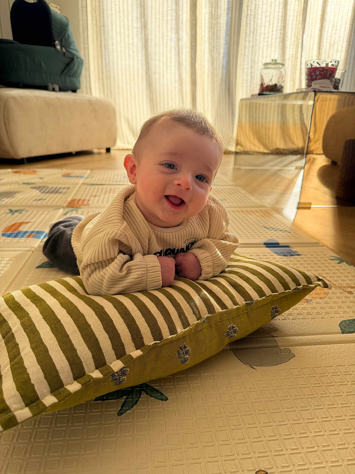 Aloïs participe au concours pour gagner de l'argent avec cette photo : baby, infant, pillow, striped_pillow, floor_mat, indoor, natural_light, smiling, tummy_time, child, cozy, curtains, furniture, home, cute, person, sweater, happy, head, playtime