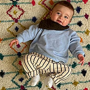 Aloïs participe au concours pour gagner de l'argent avec cette photo : baby, child, smiling, blue_sweater, striped_pants, white_socks, patterned_rug, colorful, indoor, cute, happy, portrait, infant, person, laying_down, cozy, small_hands, small_feet, head, face