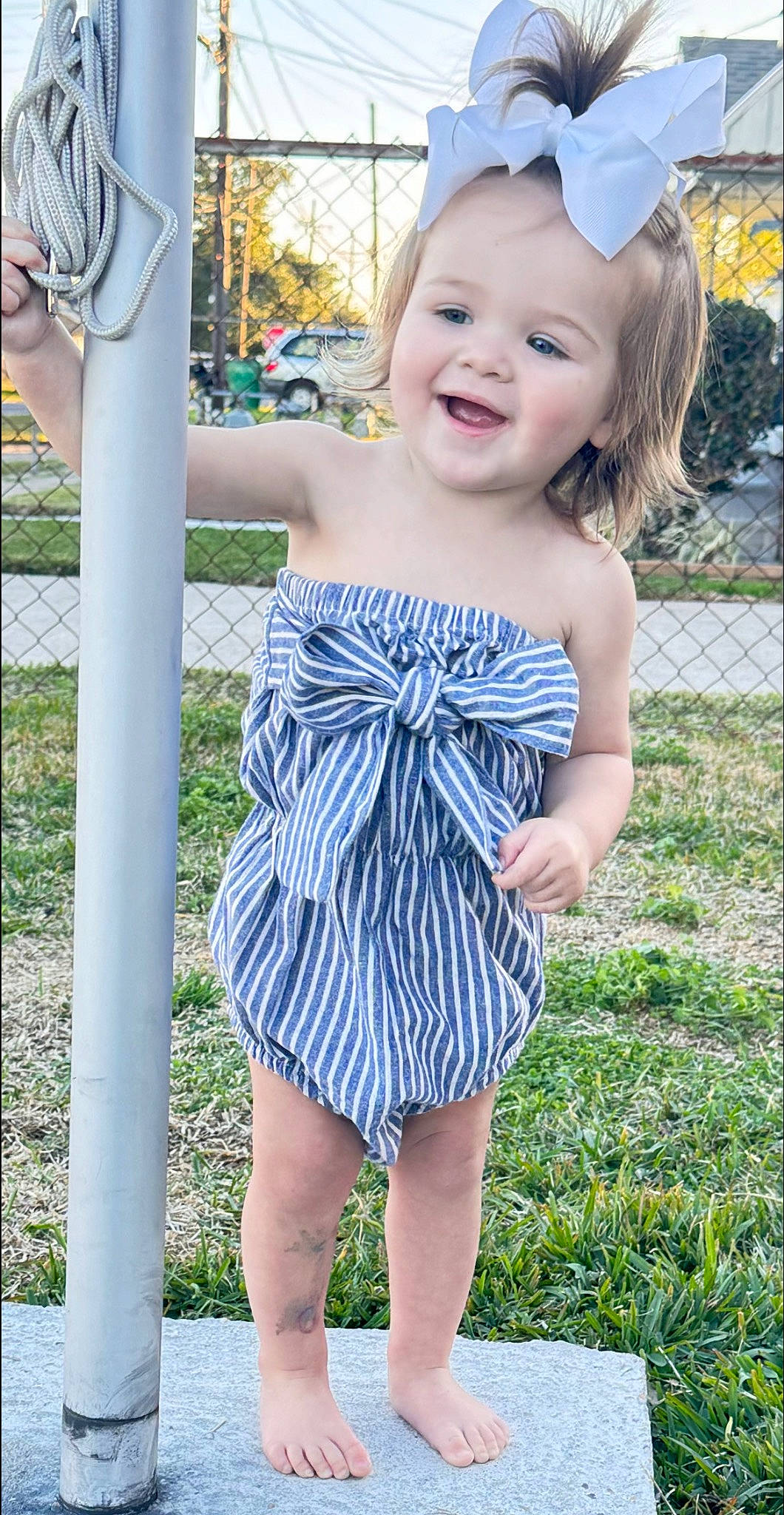 Oakley is registered to the contest to win money with this photo: baby_toddler_clothing, blue, child, dress, eye, facial_expression, hairstyle, happy, head, joy, one_piece_garment, person, photograph, plant, skin, sleeve, smile, standing, summer, waist