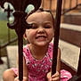 child, girl, smile, braids, pink_dress, iron_bars, outdoor, stairs, happy, portrait, cute, holding, young_child, playful, fence, daylight, person, expression, casual, background_blur