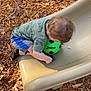 child, toddler, slide, green_ball, soccer_ball, playground, wood_chips, autumn, leaves, hair, shorts, socks, shirt, playing, outdoors, candid, seat, fun, ground, kid_playing