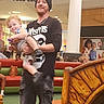 man, child, toddler, indoor, mall, play_area, beanie, tshirt, smile, bridge, water_feature, seating, casual_clothing, carrying, person, floor, pillar, background, footwear, happy