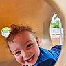 child, toddler, smiling, blue_shirt, playground, tunnel, curly_hair, happy, outdoor, face, play, young_child, candid, cute, joyful, fun, daylight, skin, person, expression