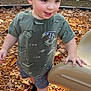 child, toddler, boy, smile, curly_hair, tshirt, shorts, socks, playground, slide, woodchips, fallen_leaves, outdoor, fence, hand, face, cheeky_expression, walking, play, daylight