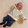 baby, infant, smile, striped_sweater, navy_pants, socks, wooden_sign, one_month, lying_down, soft_blanket, happy, cute, child, newborn, portrait, indoors, cozy, small_fists, skin, face