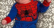 Chimmy joined the competition — help win amazing prizes! baby, blue_clothing, child, cushion, cute, face, fist, furniture, happy, head, indoor, infant, joyful, lying_down, patterned_cushion, person, playful, red_clothing, smiling, spiderman_costume