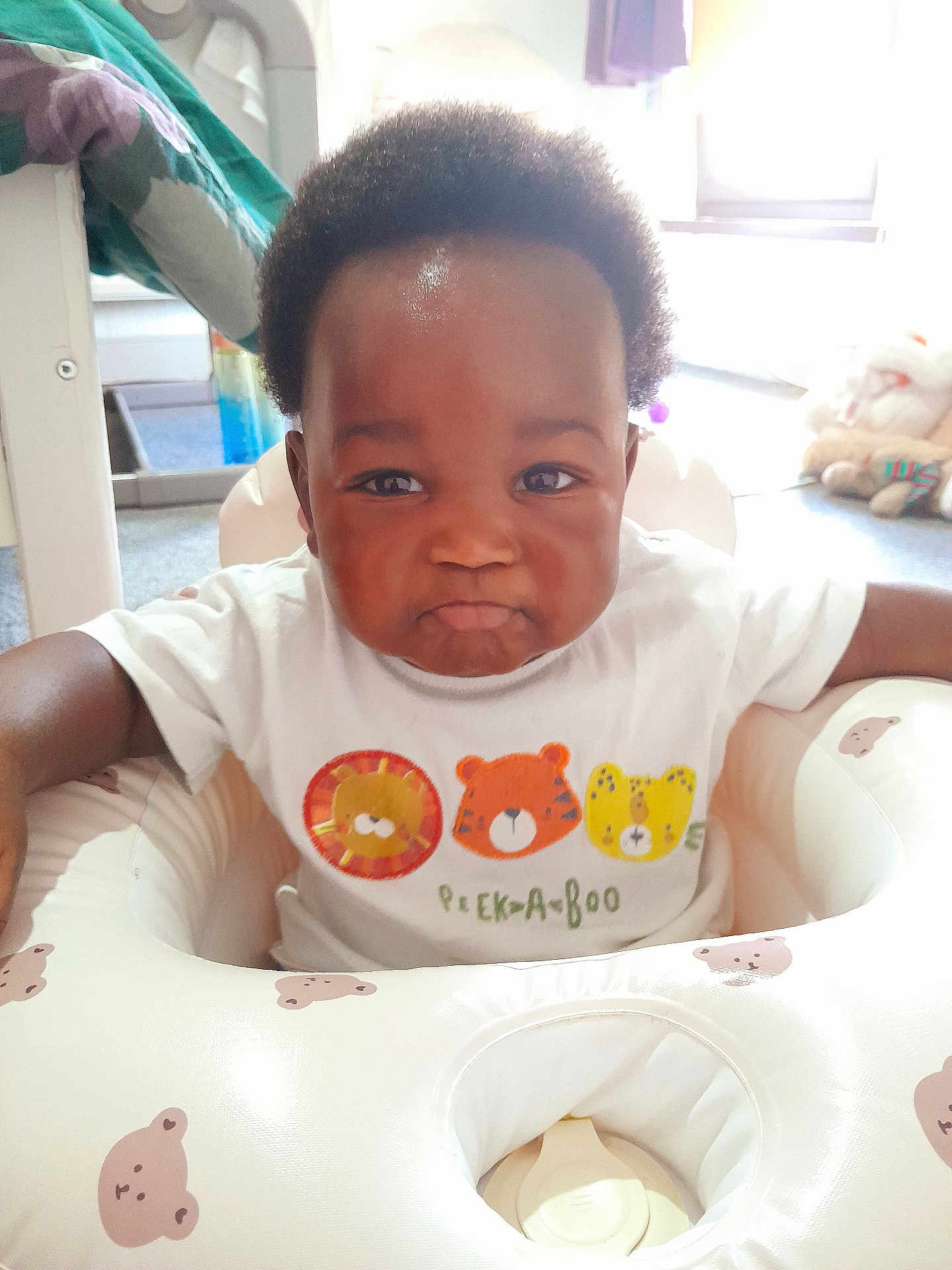 David is registered to the contest to win money with this photo: baby, child, infant, pout, white_shirt, animal_print, peekaboo_text, baby_seat, bear_pattern, indoor, toys, carpet, furniture, cute, portrait, young_child, happy, smiling, person, home
