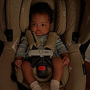 Ayla is registered to the contest to win money with this photo: baby, car_seat, infant, child, seatbelt, socks, clothing, indoor, face, person, safety, straps, expression, curly_hair, pout, looking_away, soft_lighting, beige, fabric, cushion