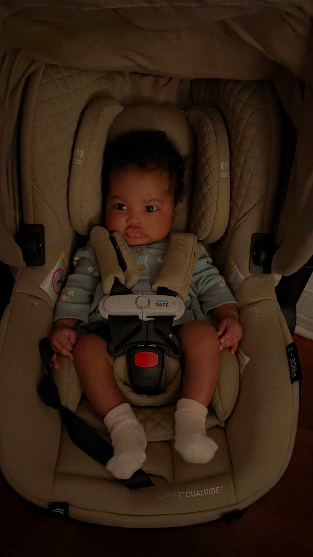 Ayla is registered to the contest to win money with this photo: baby, car_seat, infant, child, seatbelt, socks, clothing, indoor, face, person, safety, straps, expression, curly_hair, pout, looking_away, soft_lighting, beige, fabric, cushion