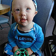 Nelson is registered to the contest to win money with this photo: toddler, child, blue_eyes, headband, toy, green_toy, levis, blue_clothing, camouflage, pants, indoor, chair, table, carpet, person, baby, sitting, curious, face, cute
