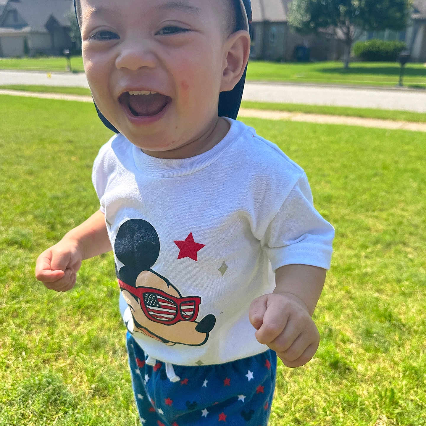 Uy-Thanh Louis is registered to the contest to win money with this photo: toddler, child, smiling, laughing, outdoor, grass, sunny, cap, tshirt, mickey_mouse, pants, stars, shoes, happy, cute, person, daylight, suburb, background, portrait