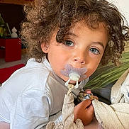 Zion a rejoint le concours — aidez-le/la à gagner de superbes lots ! toddler, child, curly_hair, blue_eyes, pacifier, plush_toy, blanket, indoor, soft_lighting, close_up, cute, cozy, person, infant, comfort, bedroom, sleepwear, face, portrait, young_child