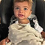 toddler, child, blanket, blue_eyes, white_shirt, black_chair, indoor, curly_hair, cushion, patterned_backrest, cute, person, young_child, soft_texture, facial_expression, seated, hand, closeup, portrait, comfortable