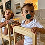 Nesta participe au concours pour gagner de l'argent avec cette photo : child, toddler, indoor, wooden_chair, pacifier, curly_hair, living_room, couch, carpet, staircase, white_clothing, furniture, person, baby, home_interior, expression, holding, sitting, playful, cute
