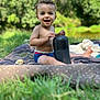 Nesta a rejoint le concours — aidez-le/la à gagner de superbes lots ! toddler, child, smiling, outdoor, grass, blanket, blue_eyes, curly_hair, speaker, picnic, nature, sunlight, happy, bare_chest, shorts, toy, greenery, park, sitting, daytime