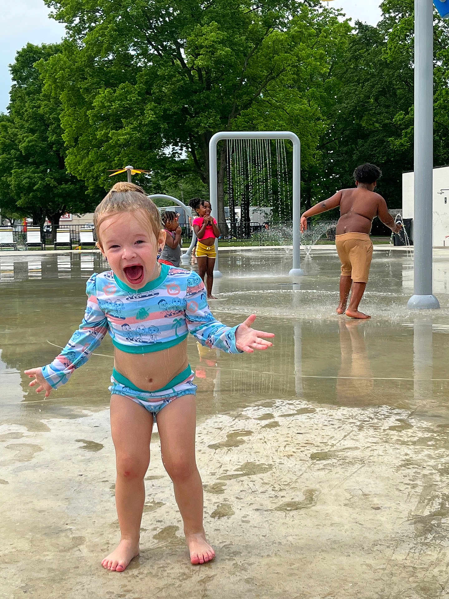 Scarlett is registered to the contest to win money with this photo: child, water_park, swimsuit, splashing, playground, water, trees, summer, outdoor, happy, barefoot, kids, fun, play, joy, park, wet, people, daytime, excitement