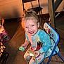 Scarlett is registered to the contest to win money with this photo: child, smiling, pajamas, chair, indoor, happy, toy, pacifier, food, snack, s'more, small_chair, colorful_clothing, playful, missing_teeth, floor, stickers, warm_light, person, cute