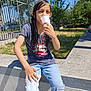 blue_sky, casual_clothing, child, concrete, daytime, fence, grass, hand, jeans, outdoor, person, plastic_cup, playful, shadow, sitting, smiling, sunlight, trees, tshirt, wet_hair