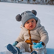 Teegan joined the competition — help win amazing prizes! baby, blue_mittens, child, cold_weather, cozy_clothing, curious, fleece, footwear, forest, hat, knit_hat, mittens, nature, outdoor, pom_poms, portrait, sitting, snow, toddler, winter