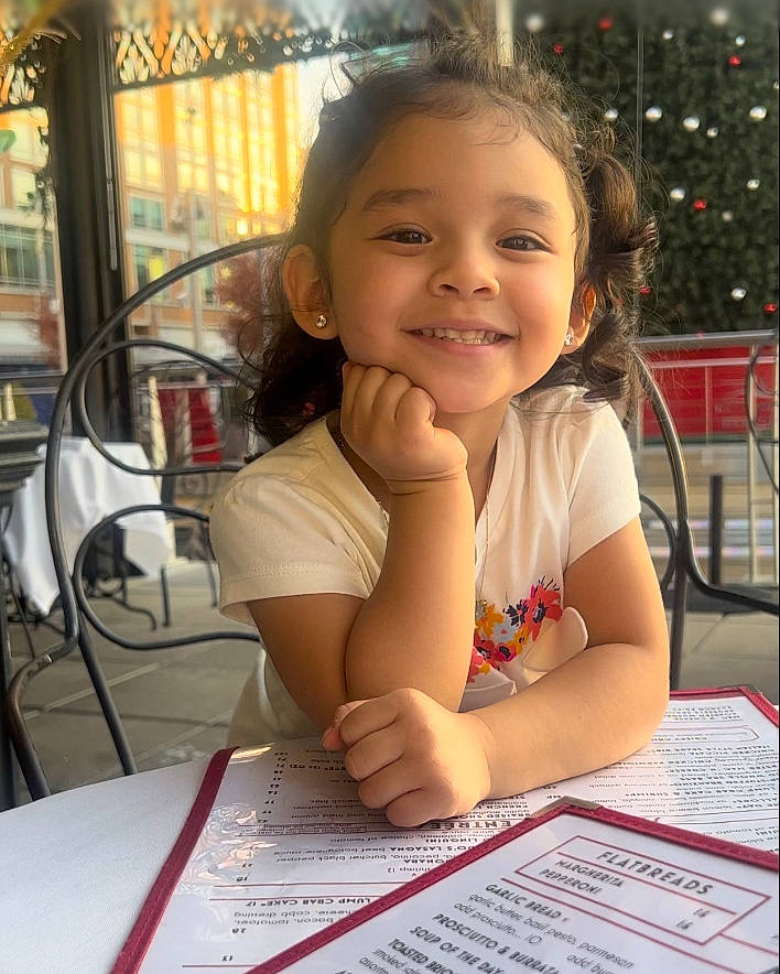 Natalia is registered to the contest to win money with this photo: chair, child, desk, fun, hairstyle, happy, joy, laugh, leisure, office_instrument, office_supplies, pen, person, sitting, smile, snapshot, table, thumb, toddler, vacation