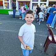Manelyo participe au concours pour gagner de l'argent avec cette photo : child, boy, smile, pastry, white_shirt, denim_shorts, white_shoes, outdoor, asphalt, people, gathering, balloons, building, window, purple_curtains, green_wall, casual_clothing, chair, daytime, social_event