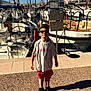 Manelyo a rejoint le concours — aidez-le/la à gagner de superbes lots ! child, boy, sunglasses, tshirt, shorts, sneakers, marina, dock, boats, sailboats, water, sunny, outdoor, daytime, shadow, sky, rope, flag, person, leisure