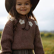 Mia joined the competition — help win amazing prizes! child, girl, smiling, hat, brown_hat, knitted_sweater, flower_pattern, long_hair, outdoor, nature, greenery, sunlight, portrait, happy, casual_clothing, plaid_skirt, standing, young, cute, warm_light