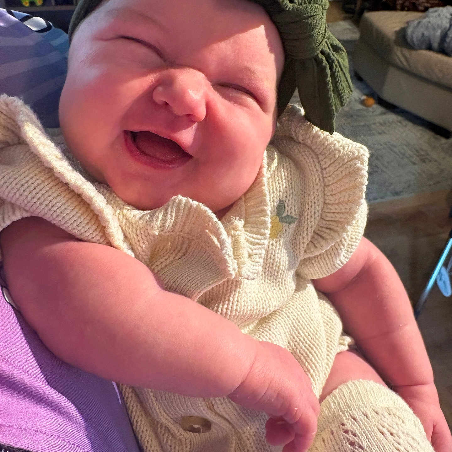 Wilder is registered to the contest to win money with this photo: baby, child, laughing, headband, knitwear, cream_color, arm, person, indoor, living_room, couch, rug, furniture, happy, smile, cute, infant, closeup, cozy, portrait