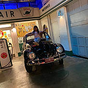 Renata Portales is registered to the contest to win money with this photo: child, car, vintage_car, gas_station, gas_pump, sign, license_plate, indoor, lighting, pose, smile, vehicle, black_car, floor, door, wall, person, automobile, headlamp, retro
