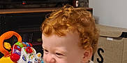 Léon a rejoint le concours — aidez-le/la à gagner de superbes lots ! baby, carpet, child, clothing, curly_hair, furniture, hand, happy, indoor, laughing, living_room, person, playful, red_hair, smiling, storage_box, table, television, toddler, toy
