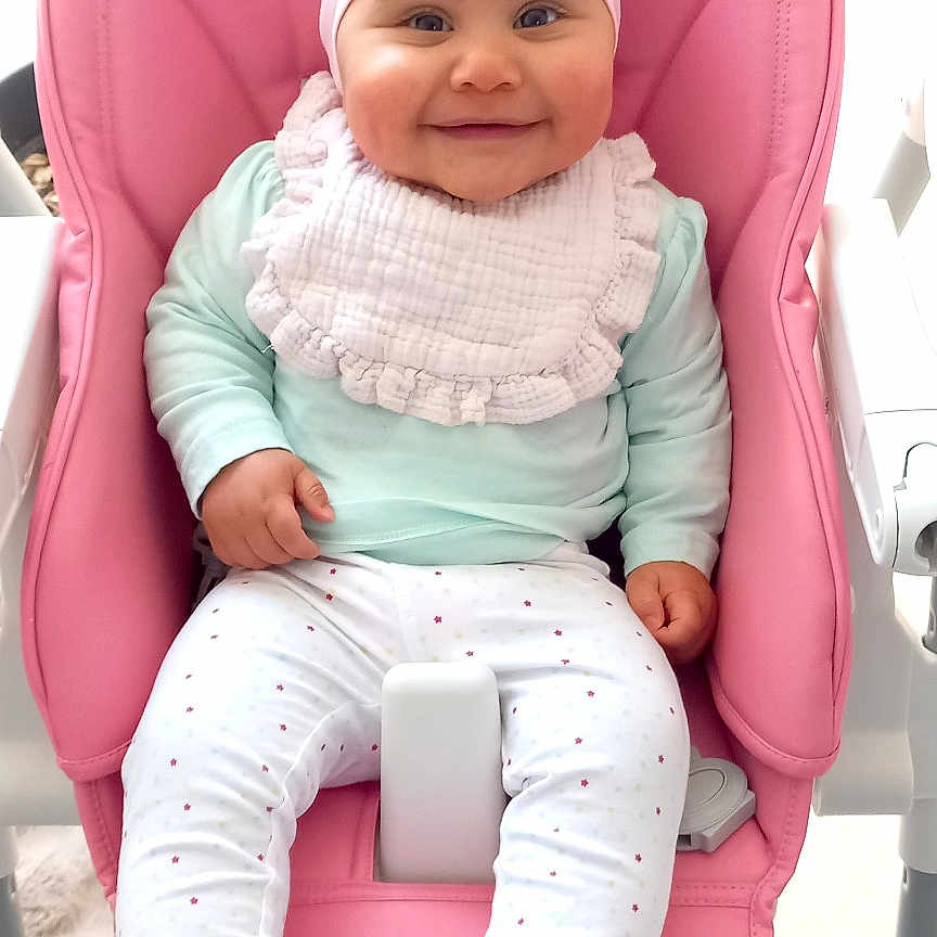 Lou a rejoint le concours — aidez-le/la à gagner de superbes lots ! baby, bib, booties, child, clothing, cute, furniture, happy, headband, high_chair, indoor, infant, pastel_colors, person, pink, plant, polka_dot, portrait, seated, smiling