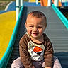 toddler, child, smiling, playground, slide, outdoor, sunny, clothing, shirt, cartoon, bear, hat, blue_sky, yellow, teal, happy, sitting, casual, young_child, daylight