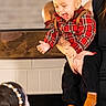 toddler, child, laughing, plaid_shirt, red_clothing, orange_socks, adult_hand, indoor, mirror, reflection, woman, black_clothing, headband, pearl_headband, joy, happiness, person, smile, holding, home