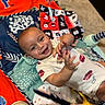 baby, smile, child, play_mat, colorful, happy, infant, clothing, pattern, toy, indoor, person, cute, lying_down, hand, face, cheerful, young_child, fabric, playtime