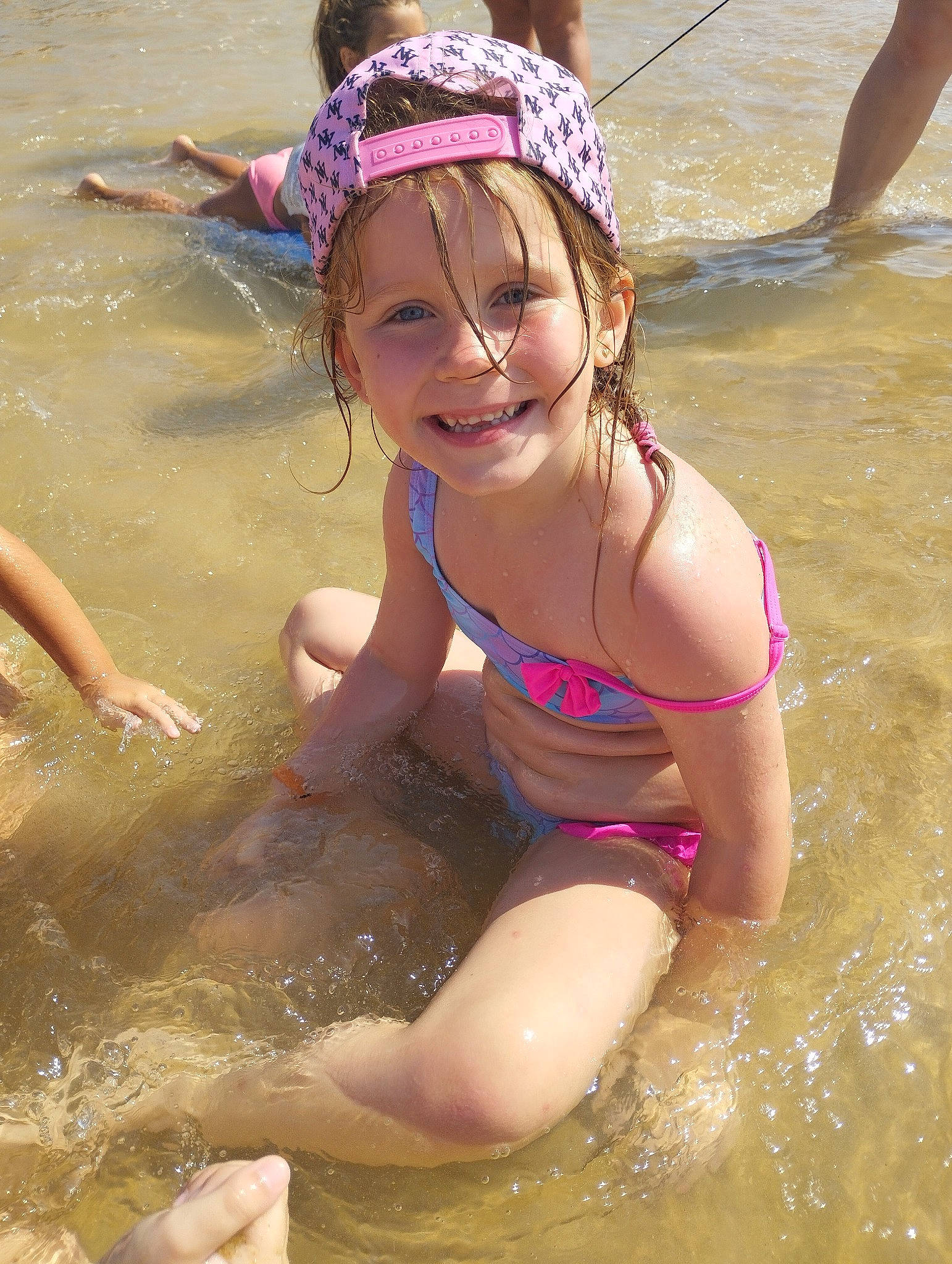Elya participe au concours pour gagner de l'argent avec cette photo : bathing, beach, body_of_water, brassiere, child, fun, happy, headwear, joy, leisure, people_on_beach, person, personal_protective_equipment, play, recreation, sand, smile, summer, swimwear, thigh