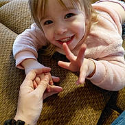 Olivia joined the competition — help win amazing prizes! child, toddler, smile, hand, holding_hands, pink_sweater, face, fingers, counting, couch, brown_fabric, indoor, person, happy, playful, home, casual_clothing, human, young_child, interaction