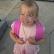 Olivia is registered to the contest to win money with this photo: backpack, blonde_hair, braids, child, concrete, dress, face, fashion, girl, happy, joy, outdoor, pink_dress, portrait, railing, school, smiling, standing, teeth, toddler