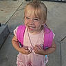backpack, blonde_hair, braids, child, concrete, dress, face, fashion, girl, happy, joy, outdoor, pink_dress, portrait, railing, school, smiling, standing, teeth, toddler