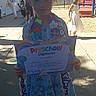 background_children, celebration, certificate, child, colorful, diploma, dress, girl, graduation, outdoor, playground, portrait, preschooler, sandals, school, school_event, smiling, standing, sunlight, trees