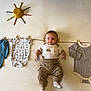 Rowan is registered to the contest to win money with this photo: baby, infant, clothing, onesie, pants, socks, crayons, bowl, clothesline, clothespins, face, smile, cute, indoor, flat_lay, creative, playful, child, young, soft_lighting