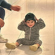 Taylor Ramos participe au concours pour gagner de l'argent avec cette photo : child, toddler, indoor, floor, tile, cap, gray_outfit, shoes, adult_hand, person, candid, playful, sitting, smile, light, shadow, wall, door, human, casual