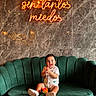 Taylor Ramos a rejoint le concours — aidez-le/la à gagner de superbes lots ! child, toddler, smiling, indoor, couch, green_couch, neon_sign, marble_wall, marble_floor, clothing, happy, sitting, shoes, toy, modern_interior, portrait, cute, lighting, decor, playful