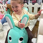 Bellarose is registered to the contest to win money with this photo: child, toy, bunny, play_area, balloons, party, indoor, smiling, happy, playful, pink_scrunchie, striped_pants, socks, furniture, floor_mat, people, background, celebration, fun, event