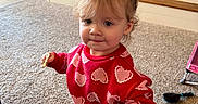 Kaylie joined the competition — help win amazing prizes! toddler, child, indoor, carpet, red_clothing, hearts_pattern, hair_buns, snack, fireplace, home, floor, cute, person, young_child, smiling, playing, cozy, warm, living_room, curly_hair